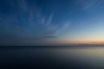 Long exposure. Evening sea under the clouds. The surface of the water turned into a flat surface. Blue sky on water reflections of the sunset. The blurred fence in the water.