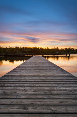 Wooden pier stretching into the lake on a background of dawn. Vertical frame