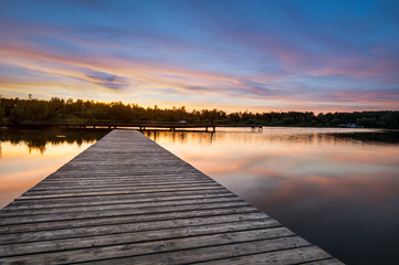Fototapeta premium Wooden pier stretching into the lake on a background of dawn. Horizontal frame