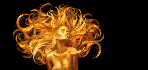 Golden beauty woman. Sexy model girl with golden makeup and long hair pointing hand over black. Metallic gold glowing skin and fluttering hair - obrazy, fototapety, plakaty
