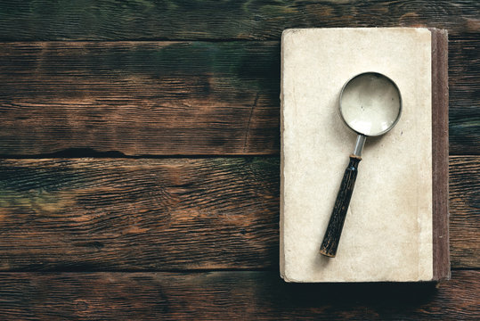 Book and a magnifying glass on a wooden table background with copy space.