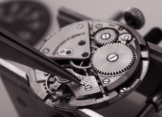 watchmaker working with tweezers into vintage mechanic watch movement