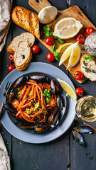 Top view Italian pasta. Mussels and vegetables. White wine. Close-up. Traditional Mediterranean cuisine. Dark wooden background