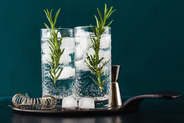 classic gin and tonic cocktail with rosemary sprigs in tall glasses on a table with bar accessories