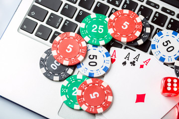 Online poker casino theme. Gambling chips with dice and playing cards on laptop.