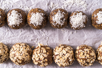 Obraz na płótnie Canvas Healthy organic energy balls made with dates, prunes, raisins, peanut, oat flakes, dried cranberries, pecan nuts, coconut shavings, on white cooking paper background.