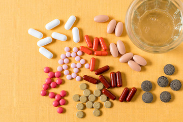 Multicolored medicine pills over yellow background.