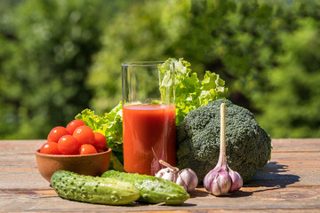 Fresh vegetables and tomato juice on old wooden table, over green nature background.