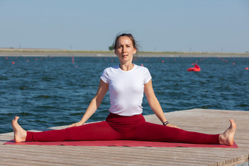 Fototapeta na wymiar Young woman doing yoga in morning park near lake