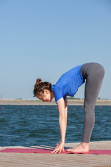 Girl practicing yoga near lake, enjoying nice day in nature and positive energy.