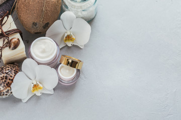 Organic cosmetics with coconut oil, sea salt, towels and handmade soap with white orchid flowers on grey background