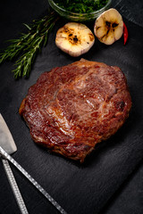 Beef grilled Rib eye steak on black stone plate with seasonings, fork and knife, meat diet