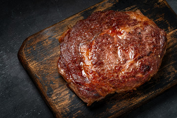Ready to eat grilled rib eye beef steak with crispy crust on wooden Board on dark background