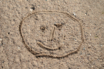 Fototapeta na wymiar A face sketched on the sand. Children's drawing drawn with a stick on a wooded road.