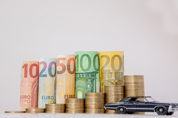 A black model of a car and ten, twenty, fifty, one hundred, two hundred and coins euro rolled bills banknotes on white background. Histogram from the euro. Concept of currency growth, savings.
