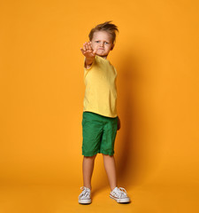 Fototapeta na wymiar Kid boy in yellow t-shirt and green shorts shows stop sign gesture on yellow
