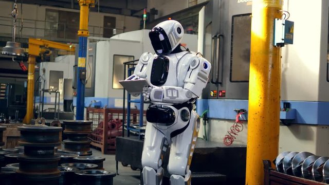 Human-like robot is working with a tablet in the factory
