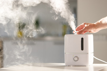 Hand turn on aroma oil diffuser on the table at home, steam from the air humidifier, free space....