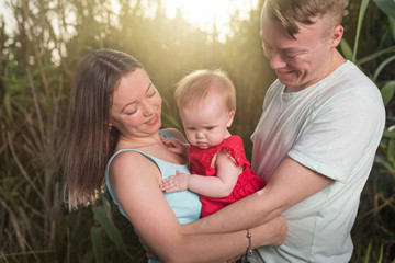 Young happy family outdoor. Parents hold child on hands and rejoice. They are happy together. Smile each other