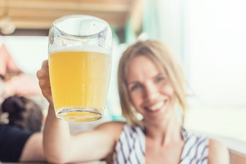 A contented smiling woman is holding a glass of cold beer in the summer on a terrace at a restaurant table.