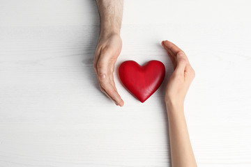 Couple holding decorative heart on white wooden background, top view