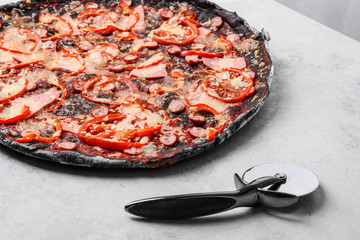 Black pizza and knife on grey table, closeup