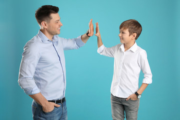 Portrait of dad and his son giving high five on color background