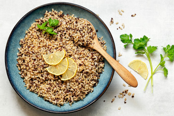 Brown rice and quinoa in a serving bowl garnished with lemon slices and parsley.