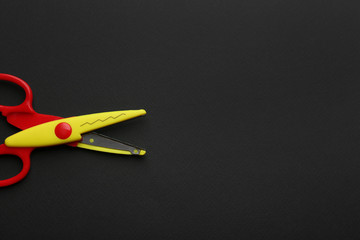 Decorative edge scissors on dark background, top view. Space for text