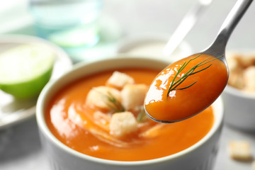 Spoon with tasty sweet potato soup over table, closeup. Space for text