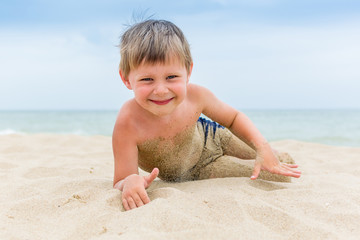 A little boy is lying on the sand in the summer. Rest of the child on the beach.