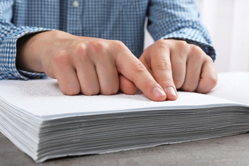Blind person reading book written in Braille at table, closeup