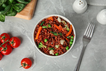 Bowl of brown rice with vegetables on grey table, flat lay