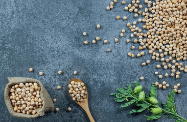 Uncooked dried chickpeas in burlap sack with raw green chickpea pod plant on rustic table. Heap of...