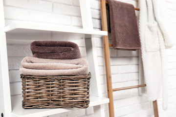 Fototapeta na wymiar Basket with clean towels on shelf near brick wall. Space for text