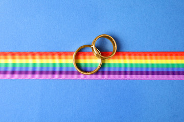 Wedding rings and rainbow ribbon on color background, top view. Gay symbol