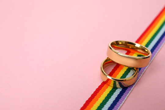 Wedding rings and rainbow ribbon on color background, space for text. Gay symbol