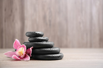 Fototapeta na wymiar Stack of black spa stones with flower on wooden background. Space for text