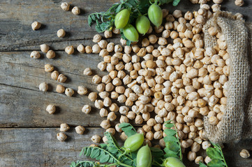 Uncooked dried chickpeas in burlap sack with raw green chickpea pod plant on wooden table. Heap of...