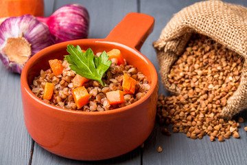 Brown bowl of tasty buckwheat porridge on gray wooden table.