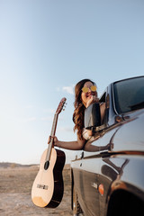 Fototapeta na wymiar Young traveler woman having fun with the guitar in the jeep 4x4 car making a wanderlust vacation at sunset