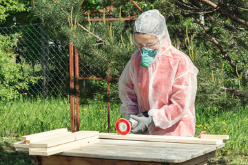 Woman carpenter in respirator, goggles and overalls handles a wooden board with a Angle grinder