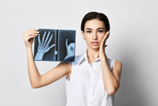Very puzzled young brunette woman holds hands X-ray examination on gray