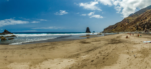 Long natural beach Benijo with footprints in the sand. Lava rock in the water. Blue sea horizon, natural sky background
