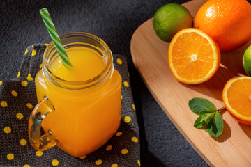 Freshly made citrus juice from oranges, grapefruit and lime in a jar-mug with a straw on black table