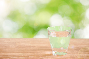 Glass of water on the table. Nature background.  Backlight addition version. テーブルの上にあるグラス一杯の水と自然背景。逆光追加版