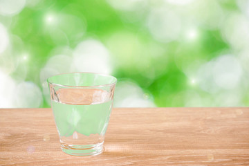 Glass of water on the table. Nature background.  Backlight addition version. テーブルの上にあるグラス一杯の水と自然背景。逆光追加版