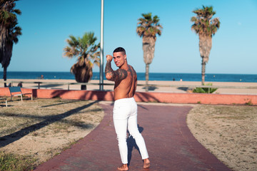 Obraz premium Tattooed bodybuilder sexy male coach at the beach. He poses for the camera and shows his muscles