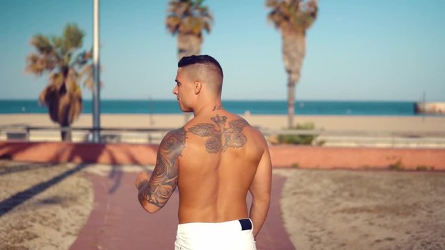 Tattooed bodybuilder sexy male coach at the beach. He stands and shows his muscles