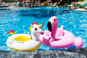 Inflatable colorful white unicorn and pink flamingo at the swim pool. Summer time in the swimming pool with plastic toys. Relaxation and fun concept